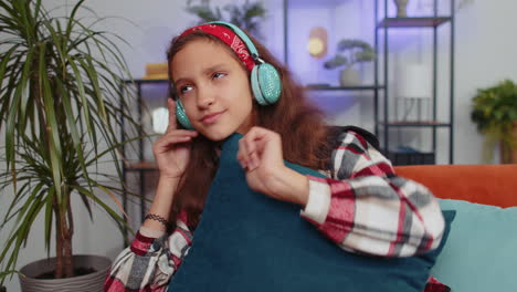 Chica-Joven-Feliz-Con-Auriculares-Inalámbricos-Relajándose-Tumbada-En-El-Sofá-En-Casa-Escuchando-Su-Música-Favorita