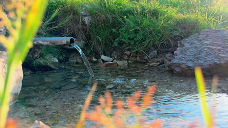 Klare-Natürliche-Mineralwasserquelle,-Die-Auf-Natürliche-Weise-Aus-Einem-Stahlrohr-In-Einen-Kleinen-Teich-Fließt,-Quellwasser