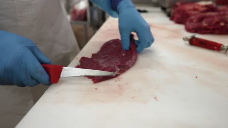 Skirt-steak-being-prepared-by-worker-with-a-knife-at-a-meat-processing-plant,-Close-up-shot