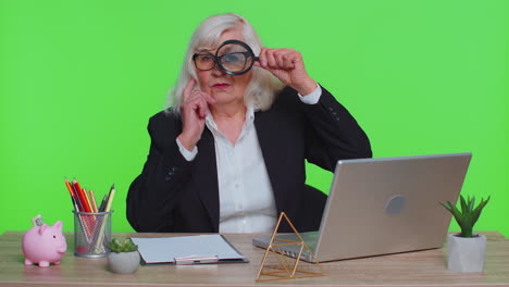 Investigator-senior-businesswoman-hold-magnifying-glass-near-face-looking-with-big-zoomed-funny-eye