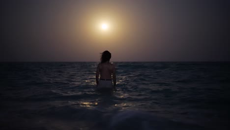 full-moon-ocean-sparkles-as-waves-gently-caress-a-serene-beach-A-man-wades-into-the-water,-enjoying-the-starlit-reflection-on-the-Persian-Gulf-tropical-paradise,-perfect-for-tranquil-exploration-iran