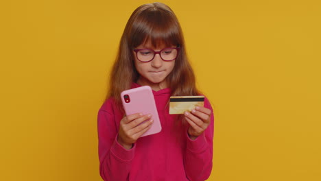 Child-girl-using-credit-bank-card-and-smartphone-while-transferring-money,-purchases-online-shopping