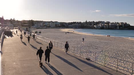 Wide-shot-of-people-walking-along-a-walking-path-at-sunrise,-Bondi-Beach