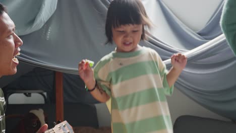 Happy-Asian-Family-Having-Fun-At-Home,-Father-Playing-Guitar-While-Mother-And-Daughter-Dancing-Together