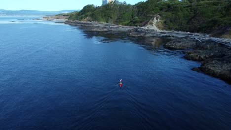 Birds-eye-view-drone-shot-kayaker-on-water-paddling-towards-beach