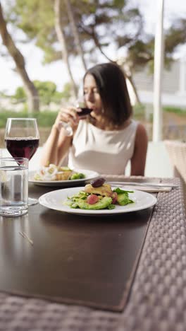 Vertical-view-of-healthy-dish-on-outdoor-table-and-woman-drink-wine,-Mallorca