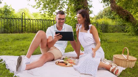 Glückliches-Paar-Mit-Tablet-PC-Beim-Picknick-Im-Park.Freizeit--Und-Personenkonzept-Glückliches-Paar-Mit-Tablet-PC-Beim-Picknick-Im-Sommerpark