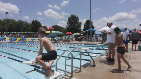 Kinder-Bereiten-Sich-Unter-Sonnigem-Himmel-Auf-Einen-Schwimmwettkampf-Vor,-Umgeben-Von-Zuschauern-Und-Trainern