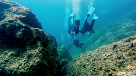 Scuba-Divers-with-dive-gear-underwater-swimming,-aquatic-exploring-sea-floor