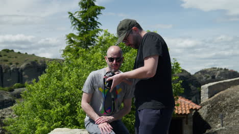 Two-male-friends-checking-their-camera-at-Meteora-monastery-windy-day