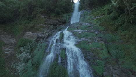 Beautiful-waterfall-in-Nepal-with-a-drone-moving-along-the-waterfall's-direction,-showing-its-source,-dense-wild-forest,-river,-and-surrounding-landscape