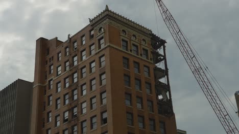 A-high-rise-building-in-Youngstown,-Ohio,-is-captured-mid-demolition-with-a-crane-in-position-and-partially-dismantled-top-floors,-highlighting-the-urban-transformation