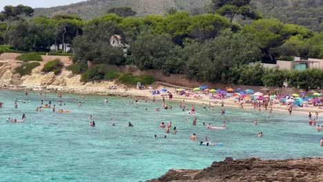 Playa-Llena-De-Gente-En-Mallorca-Con-Gente-Nadando-Y-Relajándose-Bajo-Sombrillas-De-Colores