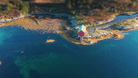 A-breathtaking-aerial-shot-capturing-a-solitary-red-cabin-on-a-remote-island-surrounded-by-crystal-clear-blue-waters-and-vibrant-underwater-vegetation