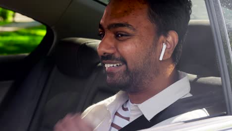 Passenger-with-Earphones-and-Cellphone-in-Taxi-Car.transport,-business-and-technology-concept-happy-smiling-indian-male-passenger-with-wireless-earphones-using-smartphone-on-back-seat-of-taxi-car