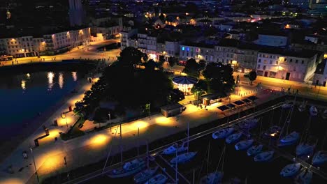 Approaching-aerial-movement-about-the-Quai-Valin-square-and-carousel-at-night,-La-Rochelle,-France