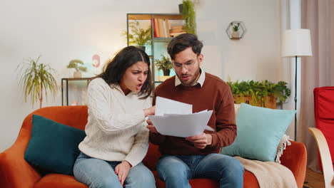 Stressed-Indian-family-looking-at-unpaid-bank-debt-bills-doing-paperwork-throws-home-paper-bills