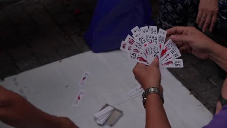 People-play-classic-card-game-Tam-Cuc-on-the-pavement,-slow-motion