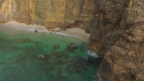 Aerial-pan-shot-of-Davids-hole-near-Baie-Rouge-beach-in-Carribean-Island-with-transparent-turquoise-water-hitting-the-rocks