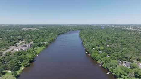 Drone-view-of-Mississippi-river-in-between-a-dense-forest-and-a-bridge-over-it-in-Minnesota,-USA