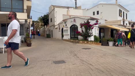 Tourists-stroll-through-a-sunny-street-in-Mallorca,-Spain,-with-shops-and-restaurants-nearby