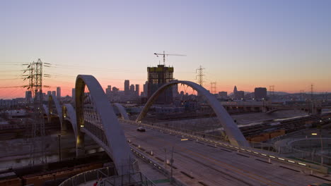 Aerial-view-of-the-6th-Street-Viaduct-bridge-in-Los-Angeles,-California,-showcasing-the-city-skyline-during-the-evening-sunset,-highlighting-the-concept-of-urban-beauty-and-transition