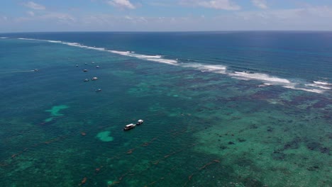 Aerial-shot-showing-boats-on-water,-seaweed-in-shallow-areas,-and-distant-waves-crashing