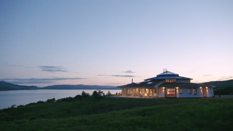 Vista-Al-Anochecer-De-Una-Casa-Escocesa-Iluminada-En-Una-Colina-Con-Vistas-Al-Sonido-De-Mull