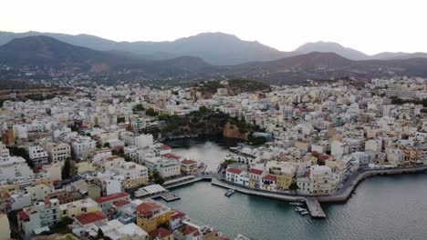 Approaching-Aerial-Panoramic-View-of-Agios-Nikolaos-Coastal-City-and-Voulisméni-Lake,-Crete,-Greece