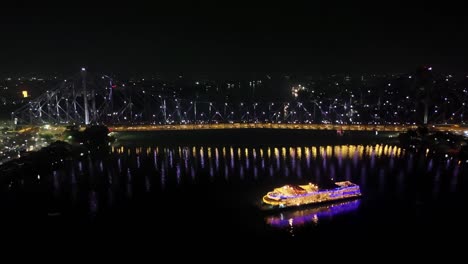 Vista-Aérea-Nocturna-Del-Famoso-Puente-Howrah-O-Rabindra-Setu-Con-Un-Hermoso-Barco-Turístico-En-Hooghly