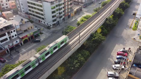 Aerial-drone-shot-of-an-electric-train-passing-by-above-a-viaduct,-in-the-middle-of-a-street