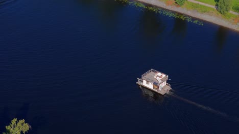 Drone-aerial-view-of-party-barge-with-people-sunbathing-moving-on-a-slow-river-in-summer-sun