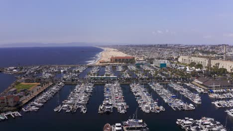 Aerial-wide-reverse-pullback-shot-of-the-King-Harbor-Marina-in-Redondo-Beach-with-Hermosa-Beach-in-the-distance-along-the-coast-in-Southern-California