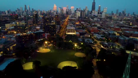 Vista-Aérea-Con-Dron-En-Hiperlapso-De-Un-Vibrante-Paisaje-Urbano-De-Chicago-Por-La-Noche,-Iluminado-Por-Deslumbrantes-Explosiones-De-Fuegos-Artificiales-A-Lo-Largo-De-Una-Bulliciosa-Calle-Principal