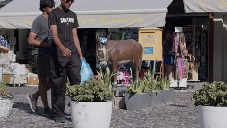 Tourist-walks-by-souvenir-shop-in-Fira,-Santorini,-Greece-with-a-donkey-statue-outside