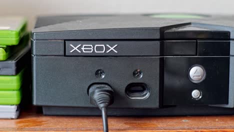 Colocar-Un-Disco-De-Juego-De-Xbox-En-Una-Consola-De-Videojuegos-Xbox-Abierta-Sobre-Una-Mesa-De-Madera-Con-Estuches-De-Juegos-De-Xbox-Al-Lado