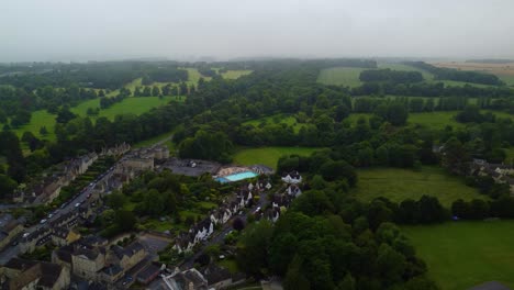 Explore-a-revealing-aerial-view-of-a-Cirencester-residential-yard-featuring-lush-green-lawns,-a-sparkling-swimming-pool,-and-charming-houses