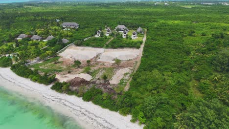 Backwards-aerial-of-rustic-lodge-in-Zanzibar-reveals-blue-turquoise-lagoon-and-white-sand-beach,-Tanzania,-Africa