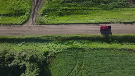 Vista-Aérea-Superior-De-Un-Automóvil-Rojo-Circulando-Por-Una-Carretera-Rural-Durante-La-Hora-Dorada-En-Dakota-Del-Norte,-EE.-UU.