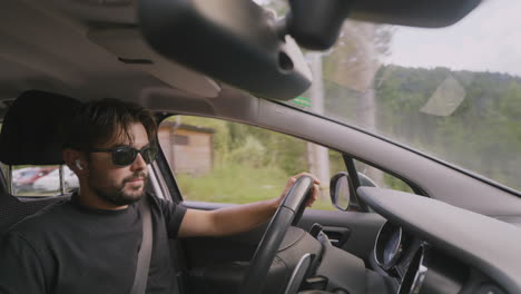 Young-man-with-sunglasses-putting-wireless-earphones-while-driving-to-answer-a-call