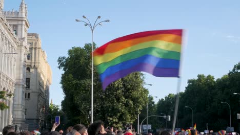 Waving-rainbow-flag-at-LGBTQ+-protest-near-a-park,-symbolising-pride-and-activism