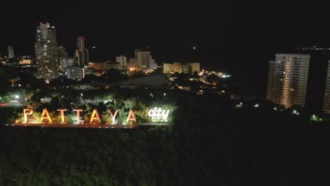 Dron-Gira-Alrededor-De-La-Ciudad-De-Pattaya,-Letrero-Iluminado-Por-La-Noche-Que-Revela-El-Horizonte-Moderno-De-La-Ciudad,-Destino-Turístico-De-Vacaciones-En-Tailandia