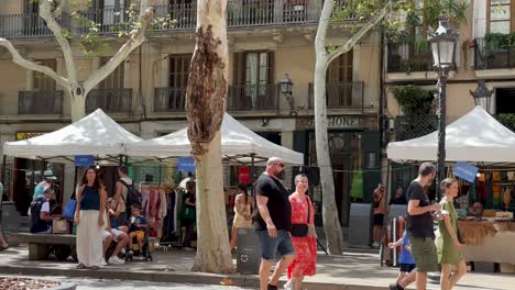 People-strolling-through-a-lively-street-market-with-white-tents-under-tall-trees-in-Born,-Barcelona