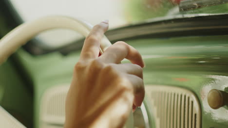 Primer-Plano-De-La-Mano-De-Una-Mujer-En-El-Volante-Conduciendo-Un-Antiguo-Coche-Verde-Retro-Tradicional-Vintage