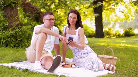 Glückliches-Paar-Mit-Smartphone-Beim-Picknick-Im-Park.Freizeit--Und-Personenkonzept-Glückliches-Paar-Mit-Smartphone-Beim-Picknick-Im-Sommerpark