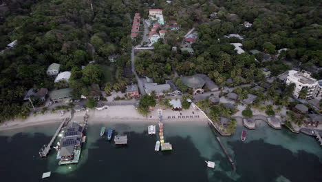 Aerial-pushback-of-the-beach-shoreline,-featuring-ocean-docks-and-boats-in-tropical-Roatan,-Honduras