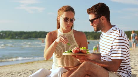 Happy-Couple-with-Food-Having-Picnic-on-Beach.leisure,-relationships-and-people-concept-happy-couple-with-food-eating-grapes-and-having-picnic-on-beach