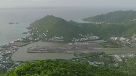 Pull-back-shot-of-Grand-Case-Airport-with-green-mountain-in-foreground-in-Saint-Martin