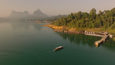 Imágenes-Aéreas-En-4k-De-Un-Barco-Que-Llega-A-Las-Habitaciones-Flotantes-En-El-Parque-Nacional-Kao-Sok-Durante-El-Amanecer,-Lago-Y-Montañas,-Tailandia,-Asia