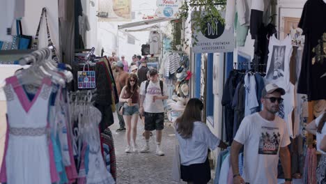 Tourists-explore-a-vibrant-street-market-in-Fira,-Santorini,-browsing-shops-and-enjoying-a-sunny-day